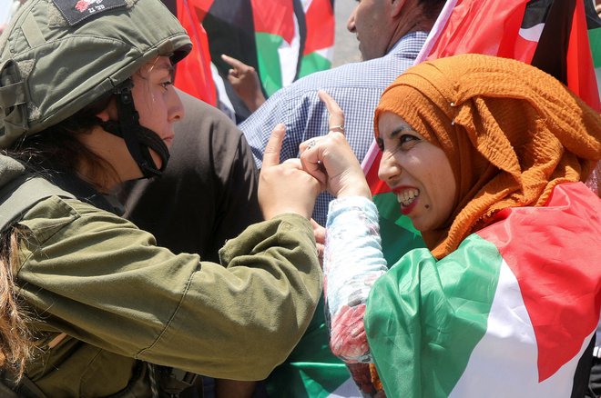 Izraelska vojakinja se prepira z demonstrantko, ovito v palestinsko zastavo, med protestom proti izraelskim naselbinam v dolini reke Jordan na Zahodnem bregu, ki ga zaseda Izrael. Foto: Raneen Sawafta/Reuters
