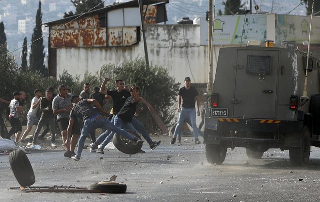 Palestinci mečejo kamenje na vojaška vozila med vojaško operacijo izraelske vojske za aretacijo iskanih oseb v taborišču Balata, v bližini mesta Nablus na Zahodnem bregu. Foto: Jaafar Ashtiyeh/Afp
