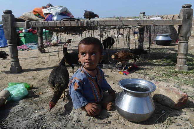 Otrok sedi na suhem v bližini svoje družine, potem ko je včeraj z družino pobegnil iz poplavljenega doma v pakistanski provinci Sindh. V Pakistanu so se okrepila prizadevanja za pomoč desetinam milijonov ljudi, ki jih je prizadelo neusmiljeno monsunsko deževje, saj je poplavilo tretjino države in zahtevalo več kot 1100 življenj. Foto: Asif Hassan/Afp
