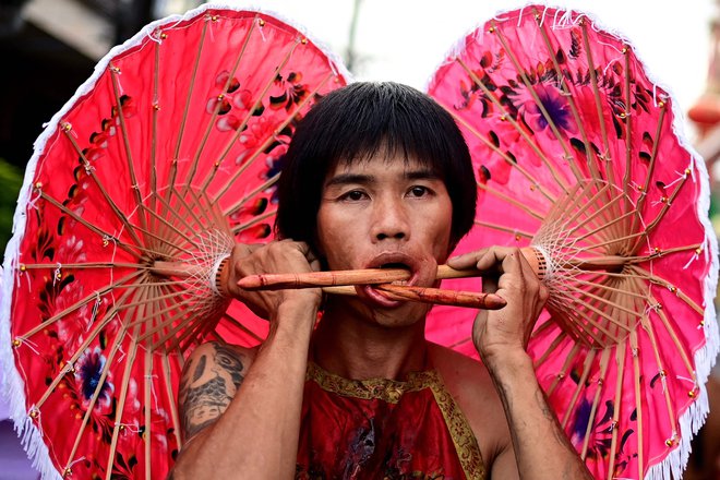 Tajski častilec svetišča Kuan Tae Kun s papirnatimi dežniki, prebodenimi skozi lica, sodeluje v procesiji med letnim vegetarijanskim festivalom v Phuketu. Foto: Manan Vatsyayana/Afp
