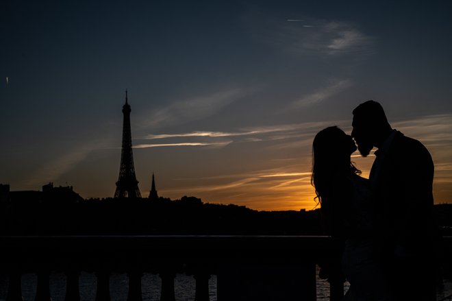 Par se poljublja ob sončnem zahodu v bližini Eifflovega stolpa v Parizu. Foto: Martin Bureau/Afp
