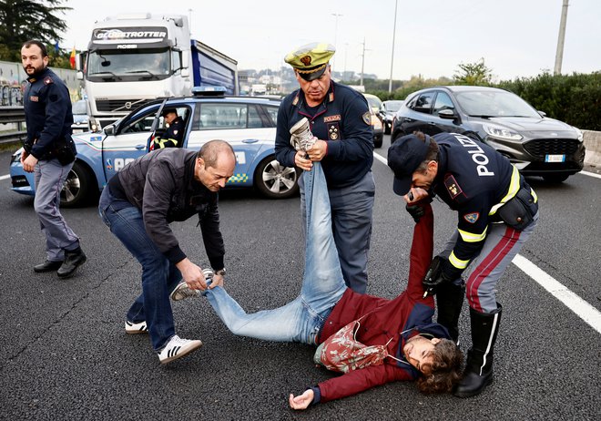 Policisti se trudijo odstraniti moškega iz ceste v Rimu, medtem ko italijanski podnebni aktivisti »Ultima Generazione« blokirajo avtocesto in opozarjajo na potrebo po boju proti podnebni krizi. Foto: Yara Nardi/Reuters
