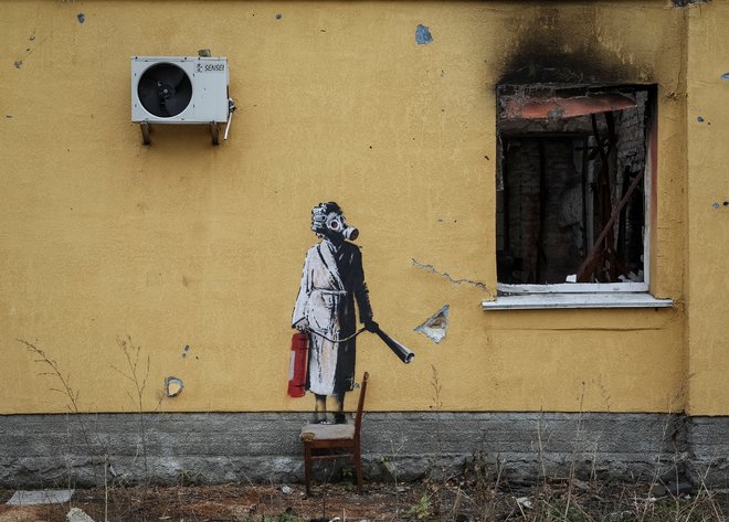 Banksy na steni v kraju Gostomel. Ženska z gasilnim aparatom in plinsko masko. FOTO: Gleb Garanich/Reuters
