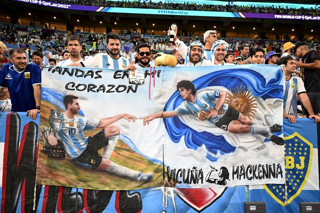 Argentinski navijači so med tekmo s Hrvaško povezali legendarna nogometaša z zastavo: levo Lionel Messi, desno Diego Maradona. FOTO: Manan Vatsyayana/AFP
