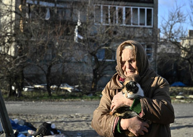 80-letna domačinka Galyna drži mačko pred poškodovano stavbo v mestu Lyman v oblegani regiji Doneck, v kateri živi brez elektrike, vode in ogrevanja. Foto: Genya Savilov/Afp
