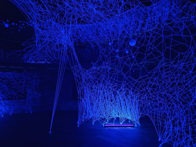 Z ultravijolično svetlobo osvetljena mreža 4000 metrov bombažnih niti je dopolnjena s 1111 visečimi kroglicami iz stiropora in plastike. FOTO: Sara Nuša Golob Grabner
