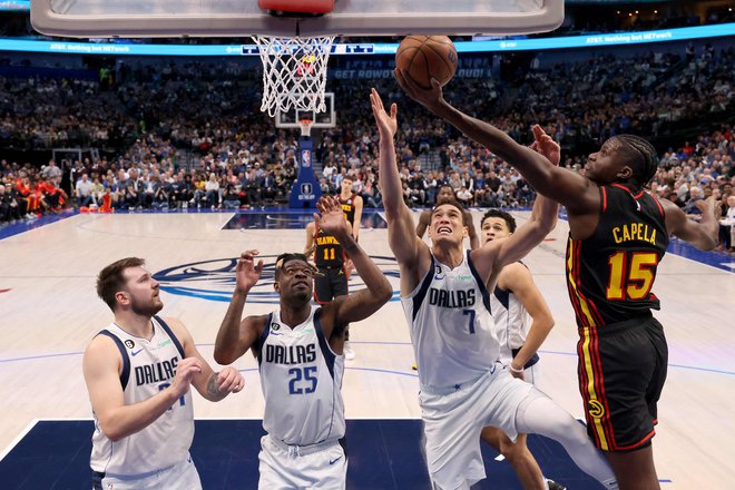 Clint Capela prodira pod koš, ustavljajo ga&nbsp;Dwight Powell, Reggie Bullock in Luka Dončić (z leve) med zadnjo četrtino dvoboja Dallasa in Atlante v&nbsp;dvorani American Airlines Center. FOTO: Tom Pennington/AFP
