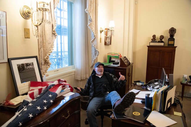 Fotografija, ki je obkrožila svet: Barnett z ameriško zastavo v roki, z nogami na pisalni mizi Nancy Pelosi. Foto Saul Loeb/AFP
