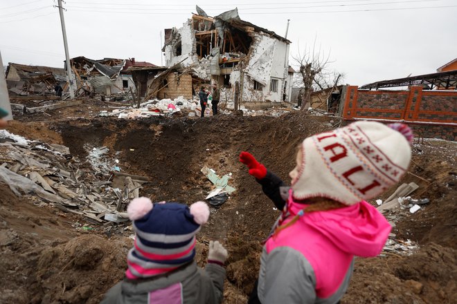 Otroka&nbsp;ob kraterju, ki ga je povzročil ruski raketni napad, v mestu Hlevaka pri Kijevu.&nbsp;FOTO: Valentyn Ogirenko/Reuter
