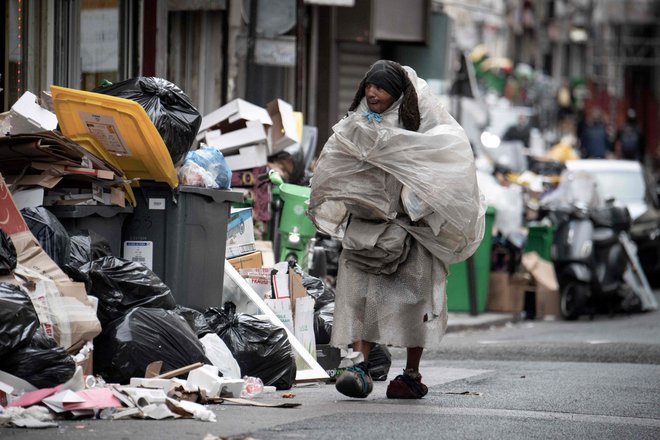 Brezdomec, pokrit s plastičnimi vrečkami, hodi mimo smeti, ki so se kopičijo na ulicah Pariza, saj delavci komunalnih podjetij že od 6. marca stavkajo proti predlagani pokojninski reformi francoske vlade. Foto: Alain Jocard/Afp
