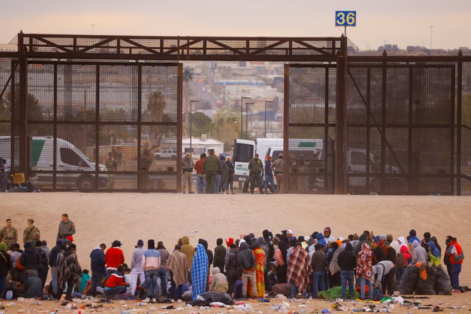 Migranti stojijo ob mejnem zidu, potem ko so prečkali reko Rio Bravo in se nameravajo predati ameriškim obmejnim patruljam na meji z ZDA. Foto: Jose Luis Gonzalez/Reuters