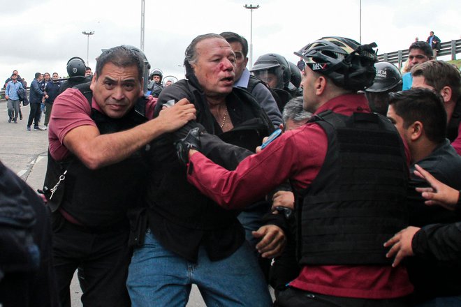 Sergia Bernija, ministra za varnost province Buenos Aires, ki ga je pretepla skupina voznikov avtobusov, na protestu zaradi umora sodelavca v La Matanzi na zahodnem obrobju Buenos Airesa, ščitijo policisti in ga peljejo na varno. 65-letnega voznika avtobusa Daniela Barrientosa, sta ustrelila napadalca, ki sta se vkrcala na avtobus, ki ga je vozil. Foto: Andres Pelozo/Afp