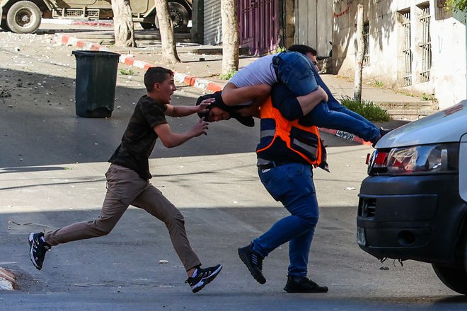 Med spopadi med izraelskimi silami in Palestinci po raciji izraelske vojske v okupiranem mestu Nablus na Zahodnem bregu zdravnik nese ranjenega moškega na varno. Izraelska vojska je akciji v Nablusu ubila tri ljudi. Foto: Zain Jaafar/Afp