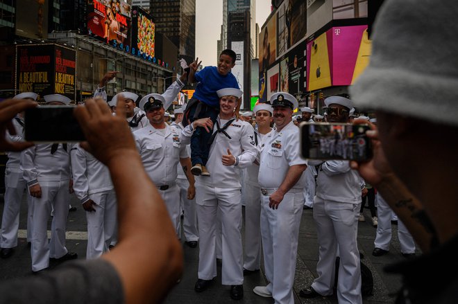 Otrok pozira s pripadniki ameriške vojske, zbranimi za skupinsko fotografijo na Times Squareu v okviru praznovanja Tedna flote v New Yorku. To je teden dni trajajoče praznovanje pomorskih služb, katerega namen je javnosti ponuditi priložnost, da na različnih dogodkih in predstavitvah spozna mornarje, marince in pripadnike obalne straže. Foto: Ed Jones/Afp