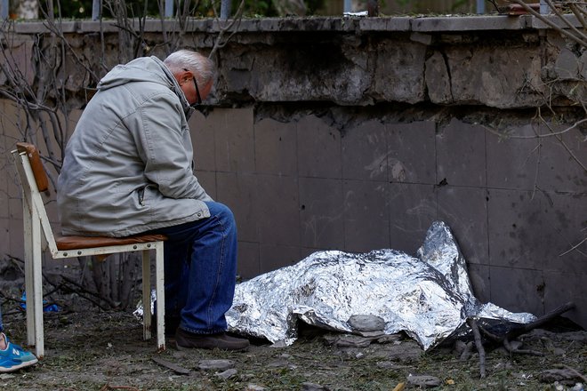 Gospod sedi ob truplu svoje vnukinje, ki je bila ubita v ruskem raketnem napadu na Kijev. FOTO: Valentyn Ogirenko/Reuters