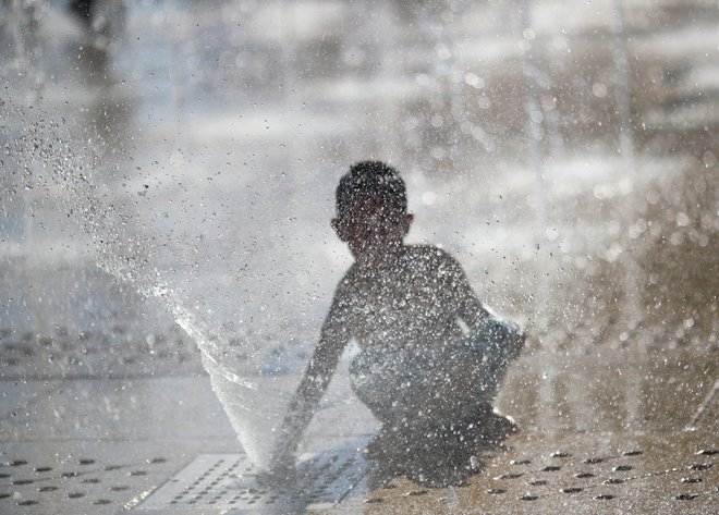 Otroci se poskušajo hladiti tudi pod vodometi. FOTO: Henry Romero/Reuters