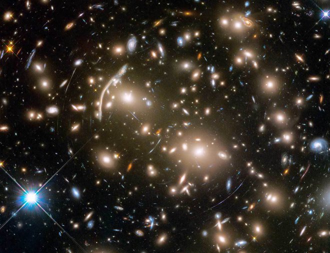 Jata galaksij Abell 370, ki je oddaljena približno štiri milijarde svetlobnih let, vsebuje osupljivo paleto več sto galaksij, povezanih z medsebojno gravitacijo. Med galaksijami so skrivnostni loki modre svetlobe, ki so pravzaprav popačene slike oddaljenih galaksij za jato. FOTO: Nasa/Esa