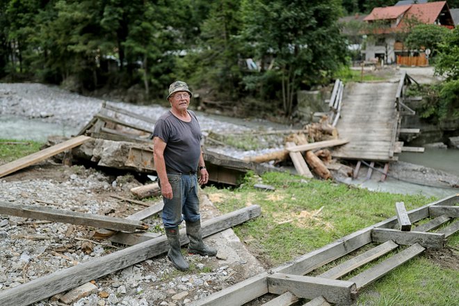 Anton Strmčnik ob podrtem mostu, ki je edina povezava s svetom ta trenutek. FOTO: Blaž Samec/Delo