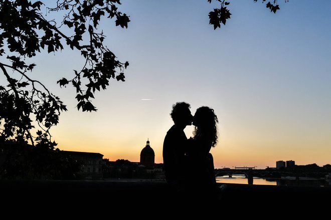 Par se poljublja ob sončnem zahodu ob bregu reke Garone v Toulusu, v ozadju pa je znamenitost Dome de la Grave. Foto: Charly Triballeau/Afp