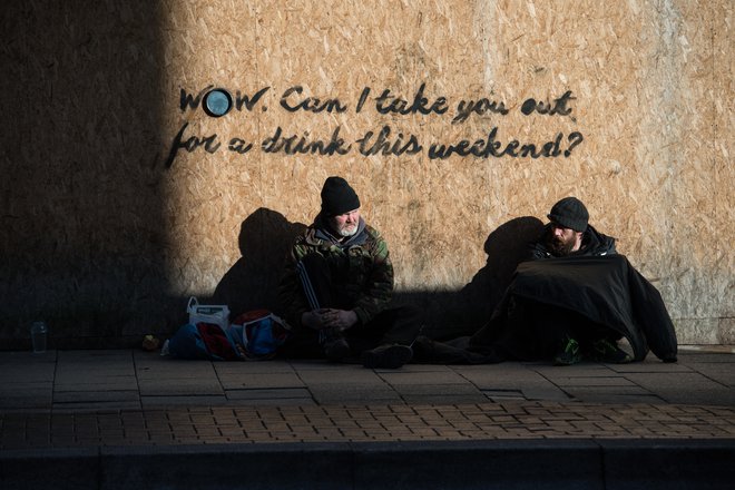 Dve osebi sedita na pločniku ob zaprti trgovini v centru Stoke-on-Trent, v osrednji Angliji. FOTO: Oli Scarff/AFP