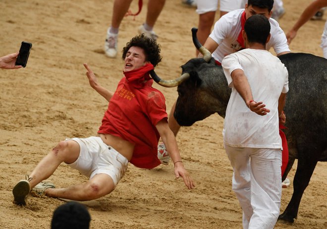 Julij 2023. Boleč utrinek iz festivala San Fermin v Pamploni na severu Španije. Tisoče ljudi se vsako leto udeleži tedenskega festivala in njegovega znamenitega »encierra« (tek pred biki). Vsak dan ob 8.00 izpustijo šest bikov, ki tečejo iz svoje ograde do arene po ozkih ulicah starega mesta na 850 metrov dolgi progi, medtem ko se tekači pred njimi trudijo ostati blizu bikov, ne da bi padli ali se podrli. Foto: Miguel Riopa/Afp