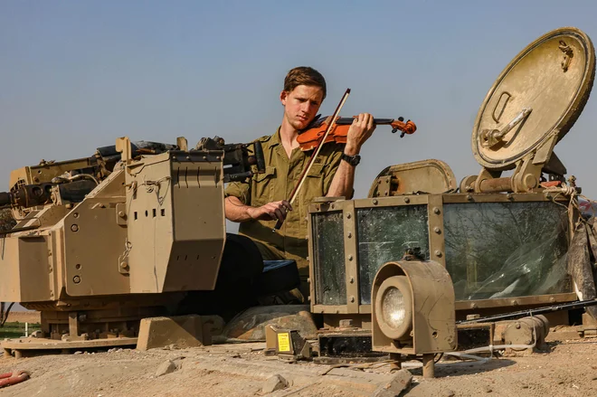 Na jugu Izraela blizu meje z območjem Gaze, izraelski vojak igra na violino na tanku. Foto: Menahem Kahana/Afp