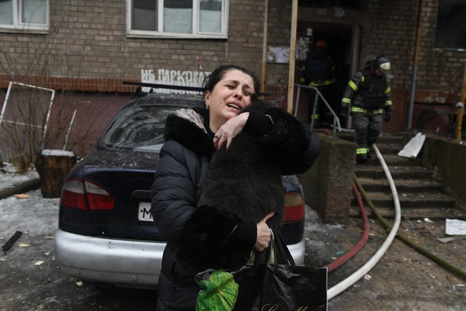 Ženska drži svojo mačko, ki so jo gasilci našli v poškodovani večnadstropni stanovanjski stavbi v Donecku, ki je bila včeraj bombardirana s strani ruske vojske. Foto: Stringer/Afp