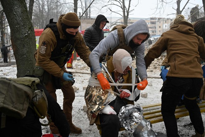 Reševalci in vojaki pomagajo poškodovanemu prebivalcu Harkova. FOTO: Sergey Bobok/AFP