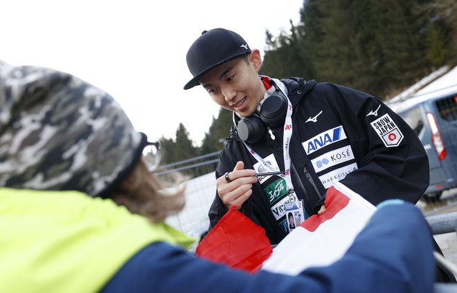 Japonski smučarski skakalec Naoki Nakamura si je med današnjim čakanjem vzel čas tudi za navijač. FOTO: Erwin Scheriau/AFP