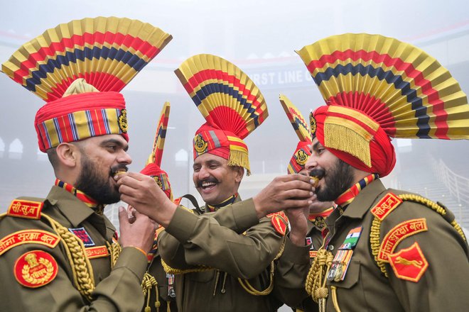 Vojaki indijskih obmejnih varnostnih sil (BSF) si med praznovanjem dneva republike na indijsko-pakistanskem mejnem prehodu Wagah, približno 35 km od Amritsarja, med seboj ponujajo sladkarije. Foto: Narinder Nanu/Afp