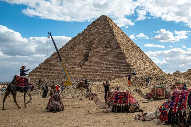 V Giizi kamele počivajo ob Menkaurjevi piramidi, zgrajeni v 26. stoletju pred našim štetjem. Mostafa Waziri, vodja egipčanskega vrhovnega sveta za starine, je v videoposnetku na Facebooku, pokazal, kako delavci postavljajo granitne bloke na osnovo piramide, in ga označil za projekt stoletja. Ko je bila piramida prvotno zgrajena, je bila obdana z granitom, vendar je sčasoma izgubila del obloge. Cilj prenove je z obnovo granitne plasti povrniti prvotni arhitekturni slog. Foto: Khaled Desouki/Afp
