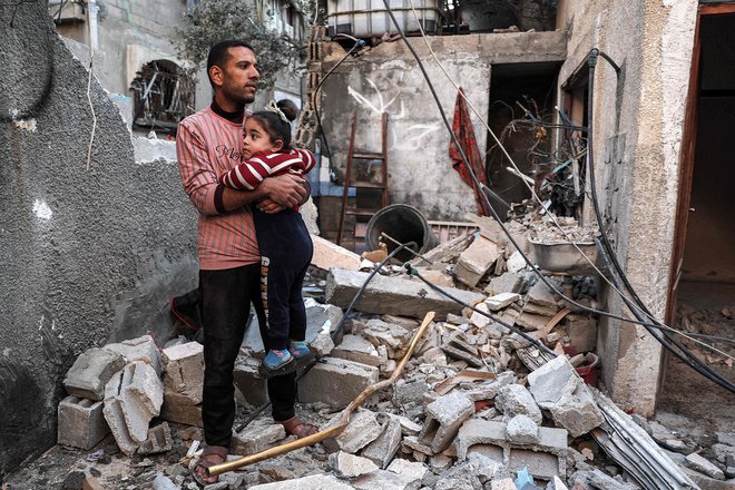 Palestinec drži v rokah deklico, stoječ na ruševinah, ki jih je povzročilo izraelsko bombardiranje. FOTO: Said Khatib/AFP