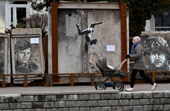 Ženska gre mimo umetnine angleškega uličnega umetnika Banksyja, ki je del razstave grafitov na prostem na osrednjem trgu Borodjanka v regiji Kijev. Umetnine mednarodnih in ukrajinskih umetnikov, ki so slikali na ruševinah porušenih stavb med rusko invazijo na Ukrajino, so lahko razstavili šele, ko so bile stavbe pozrušene. Foto: Sergei Supinsky/Afp