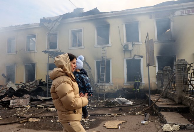 Ženska z otrokom hodi mimo uničene železniške postaje v Kostjantinivki, ki jo je zadela ruska raketa. FOTO: Anatolii Stepanov/Afp