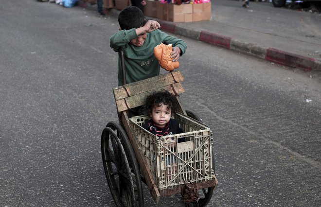 Deček potiska deklico v vozičku na ulici v Rafi na jugu Gaze. Foto: Afp