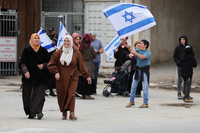 Muslimanske ženske in izraelski naseljenci v Hebronu. FOTO: Mussa Qawasma/Reuters