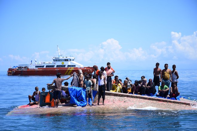 Rohinga begunci čakajo na rešitev iz trupa njihovega prevrnjenega čolna, ko se plovilo Nacionalne agencije za iskanje in reševanje približuje vodam približno 16 navtičnih milj od zahodnega Aceha. Indonezijske oblasti so rešile najmanj 69 beguncev, ki so bili tedne na morju in so jih 21. marca peljali na obalo, potem ko se je dan prej prevrnilo njihovo plovilo. Foto: Zahlul Akbar/Afp

 