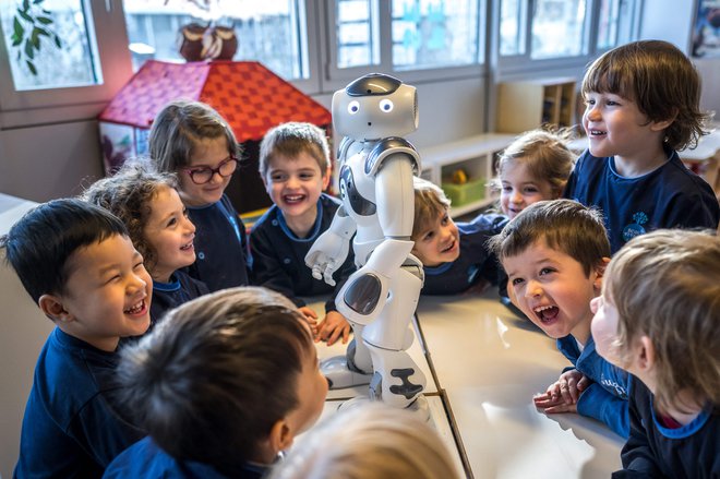 Predšolski otroci se v vrtcu v univerzitetnem kampusu Švicarskega zveznega inštituta za tehnologijo v Lozani družijo z izobraževalnim in interaktivnim robotom Nao. Nao je od novega leta redni obiskovalec vrtca Nanosphere. V krogu na tleh vrtca mladi navdušeno poslušajo Naove modrosti, ko prijazni robot z drugega planeta odgovarja na njihova vprašanja o žirafah in brokoliju. Foto: Fabrice Coffrini Afp