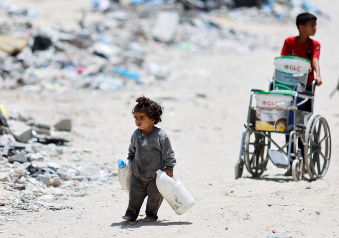 Palestinsko dekle nosi vodo, ko gre mimo hiš, ki so bile uničene v izraelskem napadu v mestu Khan Younis na jugu Gaze. Kljub petkovi odločitvi Meddržavnega sodišča v Haagu (ICC), naj Izrael nemudoma ustavi vojaško operacijo v Rafi, je izraelska vojska še okrepila napade, medtem pa na egiptovski strani propada hrana, ki bi jo morali tovornjaki s pomočjo dostaviti v Gazo. Foto: Mohammed Salem/Reuters