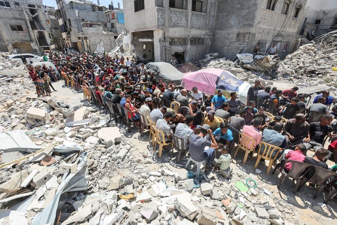 Palestinci jedo hrano, ki jo je pripravila dobrodelna kuhinja v bližini hiš, uničenih v izraelski vojaški ofenzivi, v mestu Khan Younis na jugu Gaze. Predsednik ZDA Joe Biden je povedal, da je Izrael predlagal nov celovit sporazum o prekinitvi ognja v Gazi za šest tednov, če Hamas izpusti vse talce, ki jih je zajel med napadom na Izrael 7. oktobra lani. Pozval je h koncu vojne. Foto: Ramadan  Abed/Reuters
