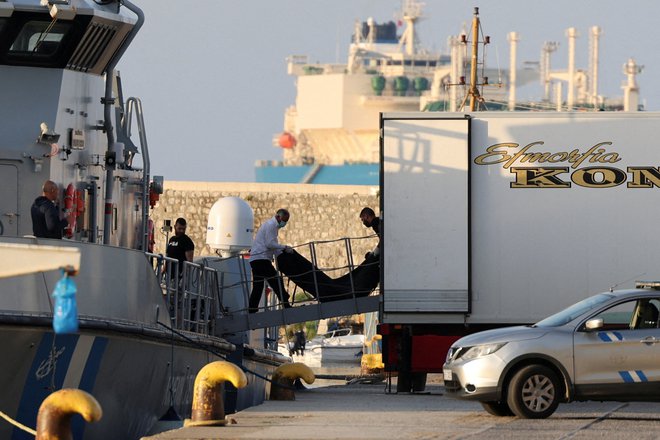 Moški prenašajo vreče s trupli migrantov, ki so umrli, ko se je njihov čoln prevrnil na odprtem morju ob Grčiji. FOTO: Stelios Misinas/Reuters