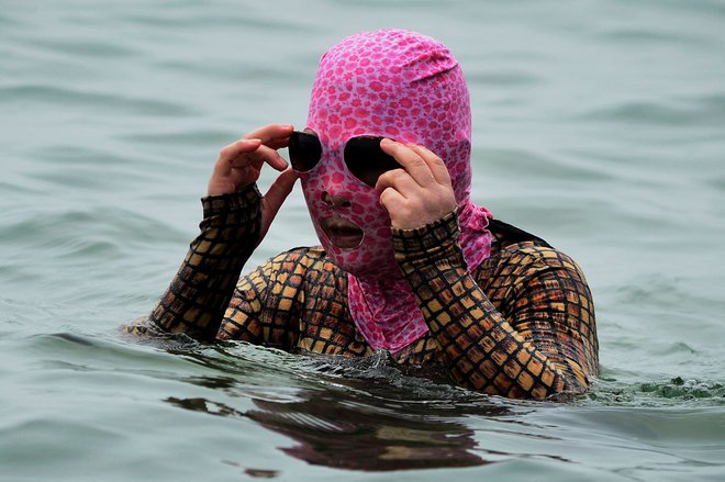 Ženska v kopalkah in z zaščitno masko se hladi na plaži v mestu Qingdao v provinci Shandong na vzhodu Kitajske. FOTO: Stringer/AFP