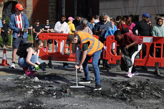 Prebivalci čistijo razbitine po izgredih. FOTO: Hollie Adams/Reuters