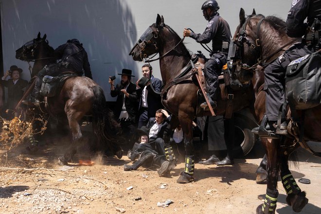 Pred vojaško bazo Tel HaShomer blizu Tel Aviva izraelska policija obkroža protestnike med demonstracijami ultraortodoksnih Judov na prvi dan, ko so morali verni judovski moški po sodni odločbi na obvezno služenje vojaškega roka. Ultraortodoksni semeniščniki, ki so bili v preteklosti izvzeti iz obveznega služenja vojaškega roka, so vpoklicani, ker izraelska vojna v Gazi in morebitni spopad s Hezbolahom na severni meji zmanjšujeta sredstva in spodbujata odpor do tistih, ki jim ni treba služiti. Foto: Oren Ziv/Afp