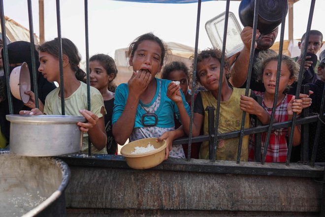 Palestinski otroci prejemajo tople obroke hrane v okviru prostovoljne pobude v začasnem taborišču za razseljence v Khan Yunisu na obleganem območju Gaze. Foto: Bashar Taleb/Afp