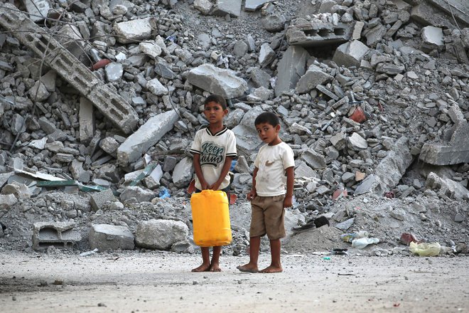 Palestinska dečka s posodo za vodo pred kupom ruševin v Nuseiratu v osrednji Gazi FOTO: Eyad Baba/AFP