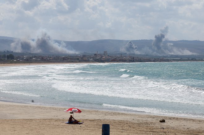 Ženska sedi na plaži v Tiru na jugu Libanona, medtem ko se iznad okolice vije dim zaradi izmenjave ognja med Izraelom in Hezbolahom. FOTO: Aziz Taher/Reuters