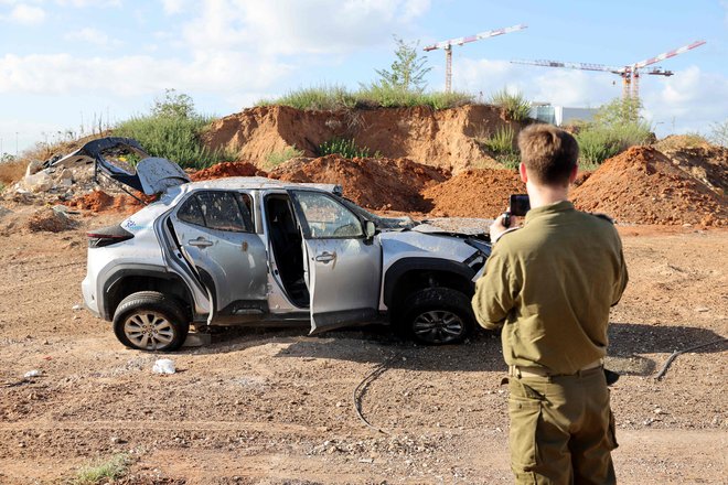 Izraelski vojak fotografira avtomobil, poškodovan v iranskem napadu na Izrael. FOTO: Jack Guez/AFP