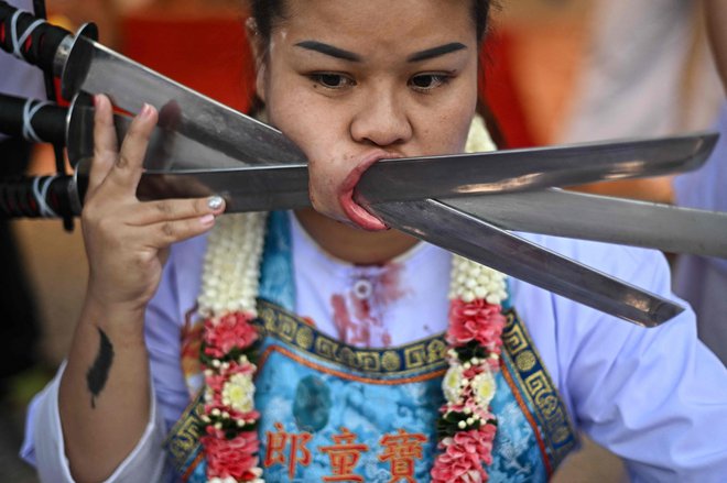 Sirinnicha Thampradit, častilka svetišča Jor Soo Gong Naka, z meči, prebodenimi skozi lice, sodeluje v procesiji med letnim vegetarijanskim festivalom na Phuketu. Na Tajskem poteka desetdnevni festival etničnih Kitajcev, med katerim se odpovejo mesu, alkoholu in spolnim odnosom, da bi očistili duha in telo. Foto: Manan Vatsyayana/Afp