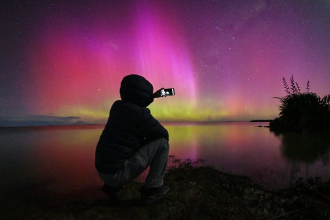 Na obrobju Christchurcha moški fotografira »auroro australis«, znano tudi kot južni sij, ki sije na obzorju nad vodami jezera Ellesmere. Foto: Sanka Vidanagama/Afp